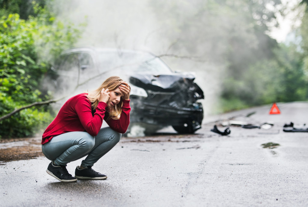 Woman on the phone in front of her damaged car after a car accident