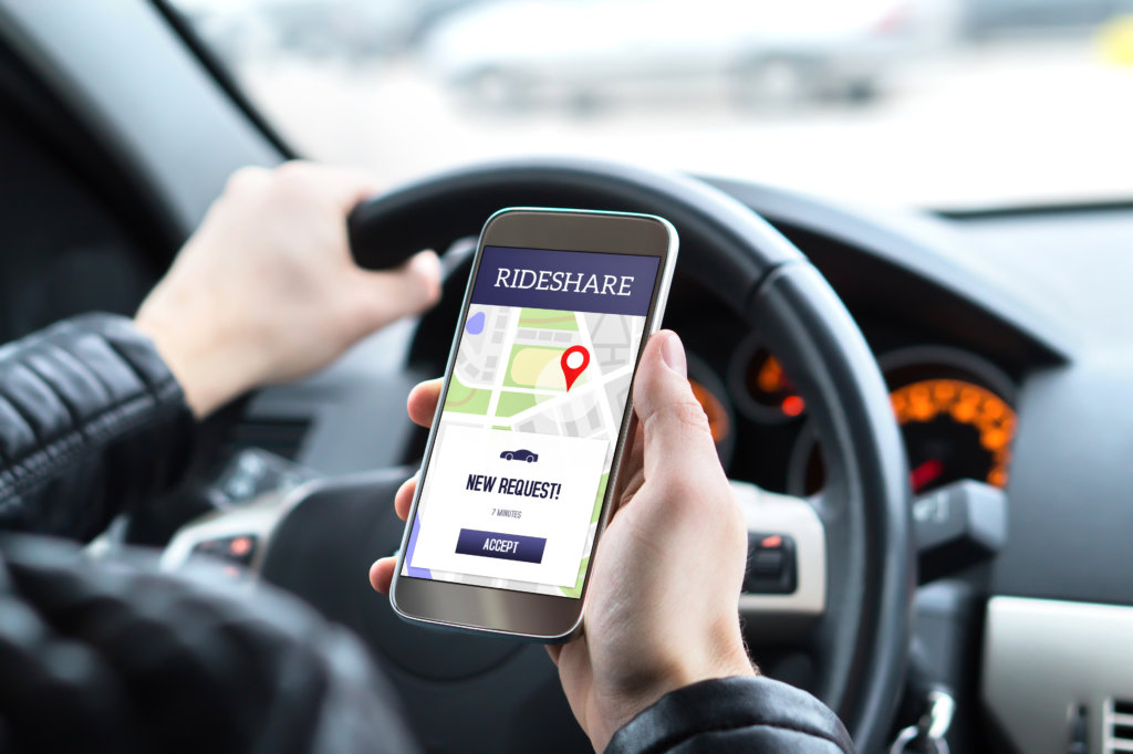 Man holding his phone displaying a ridesharing app while driving