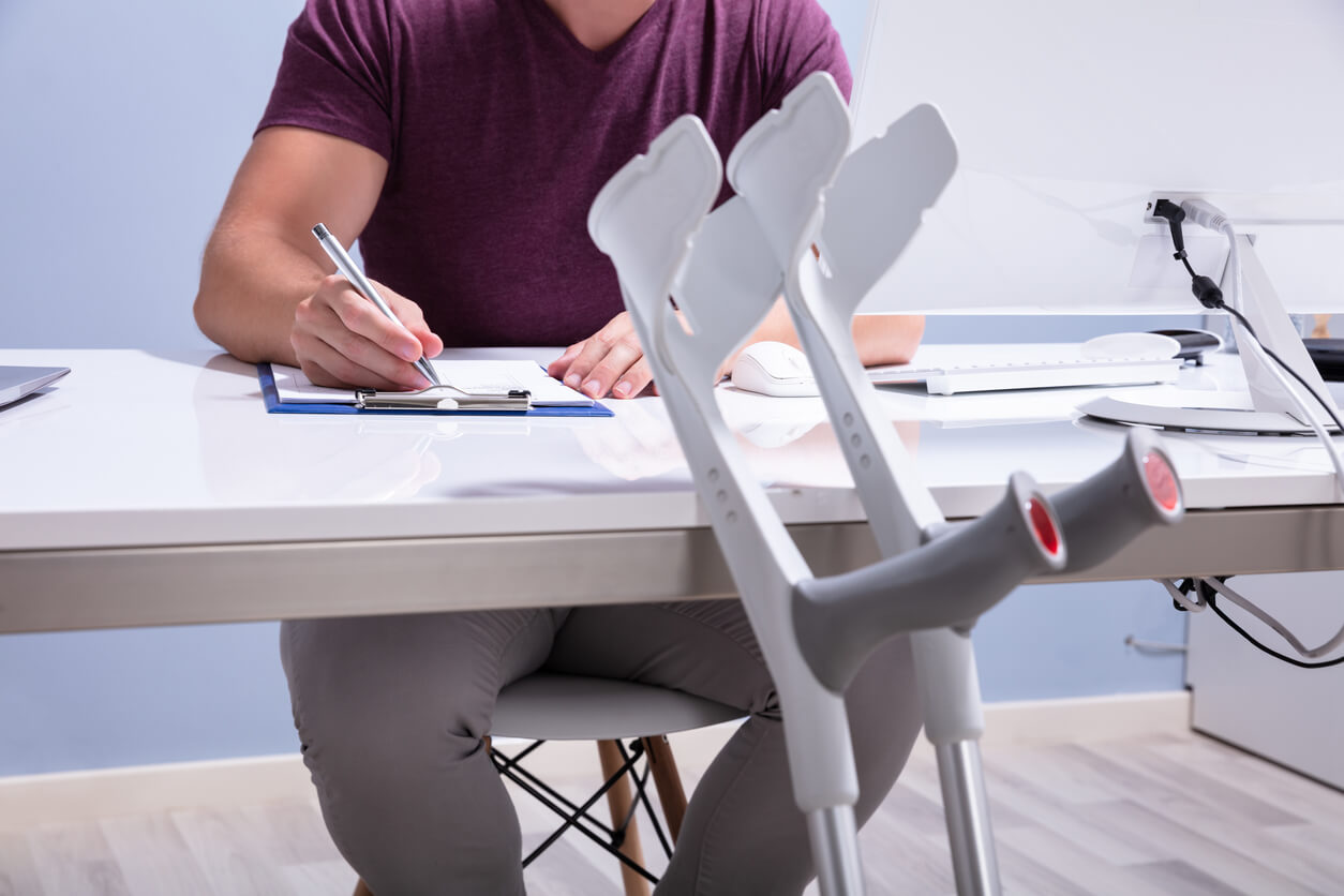 Man with crutches sitting at folding table filling out paperwork