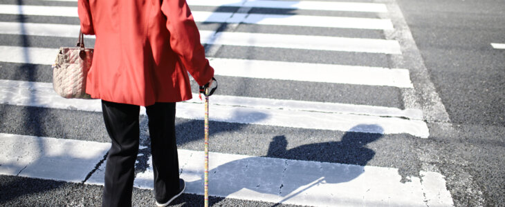 Elderly woman with a cane walking in crosswalk
